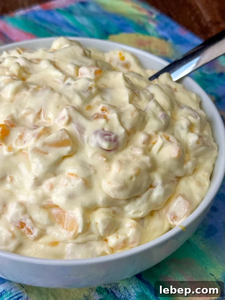 Light, creamy and fruity salad with Cool Whip in a white bowl with a silver spoon on a pastel napkin.
