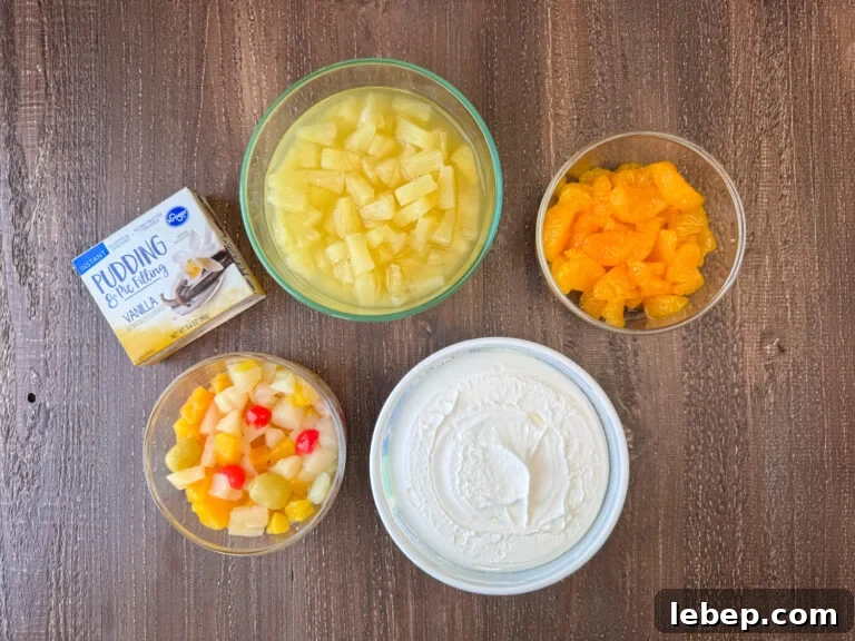 Ingredients to make fruit salad are instant vanilla pudding, pineapple tidbits, mandarin oranges, Cool Whip and fruit cocktail on a wooden counter top.