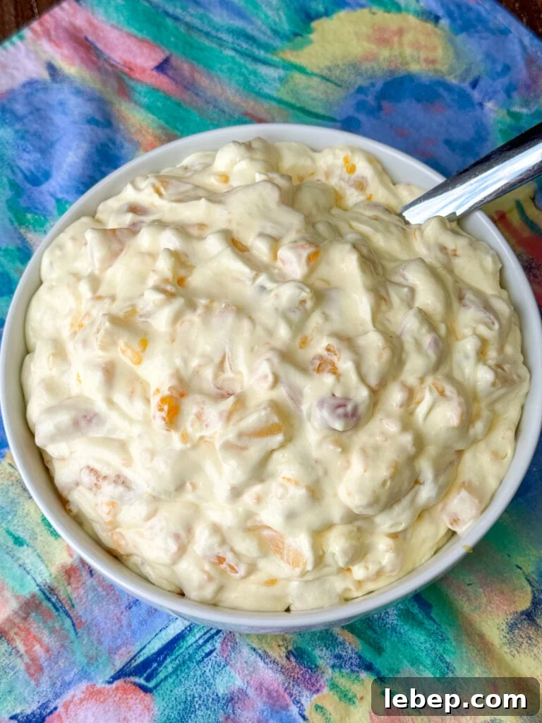 Overhead view of a serving dish of fruit salad with Cool Whip and pudding on a pastel napkin.
