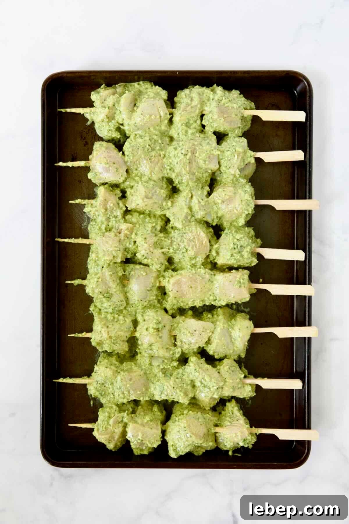 Eight uncooked chicken skewers on rimmed sheet pan.