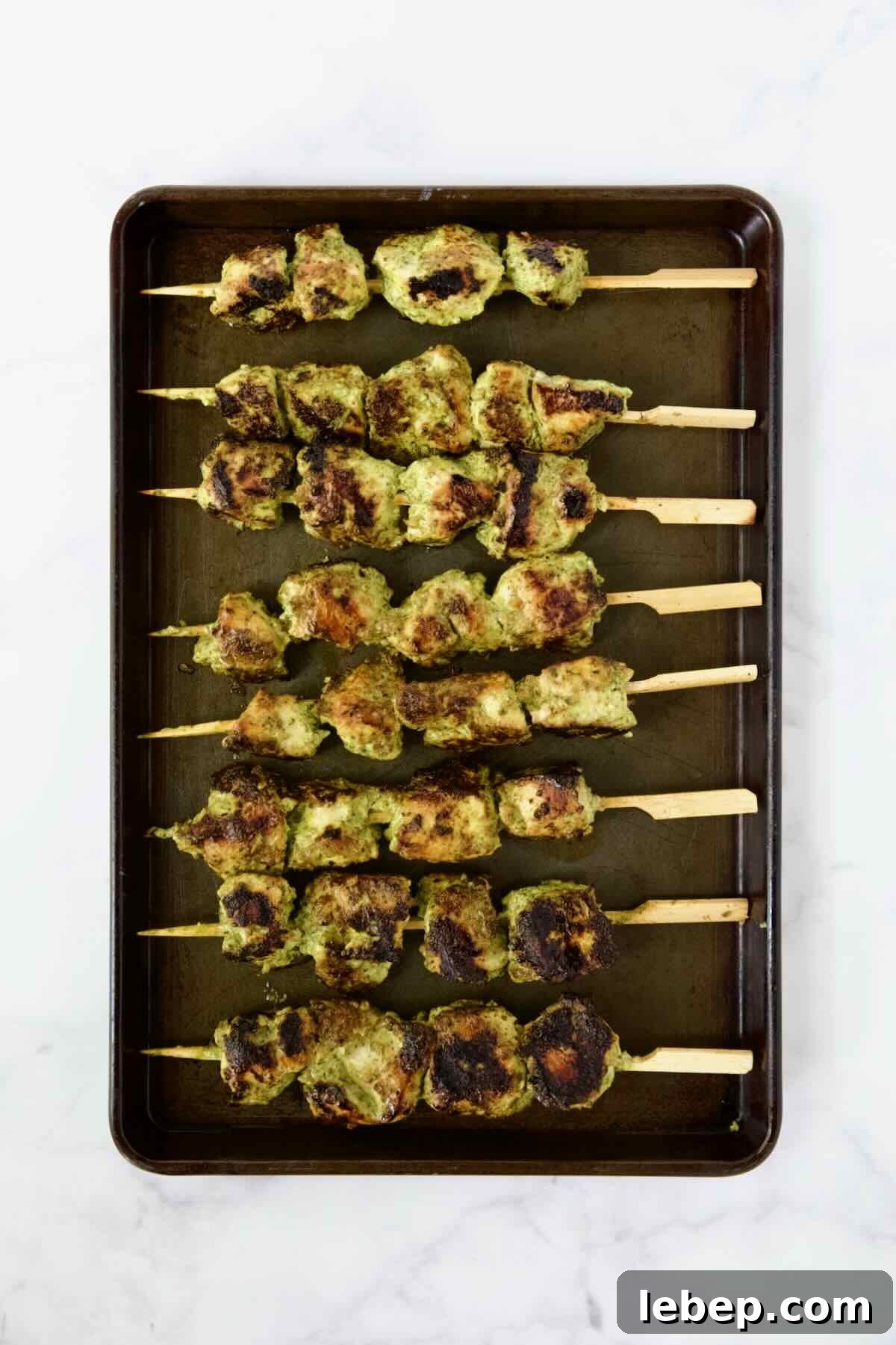 Eight grilled chicken skewers on rimmed sheet pan.