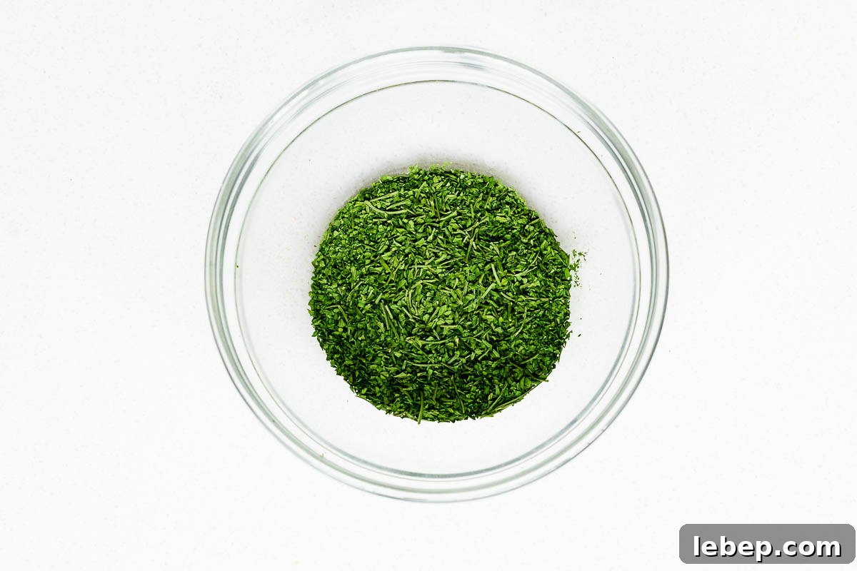 Drying Parsley in the Oven: Quick Guide for Flavorful Dried Herbs 9 Crumbled oven dried parsley with larger stems removed, in a glass bowl viewed from above.