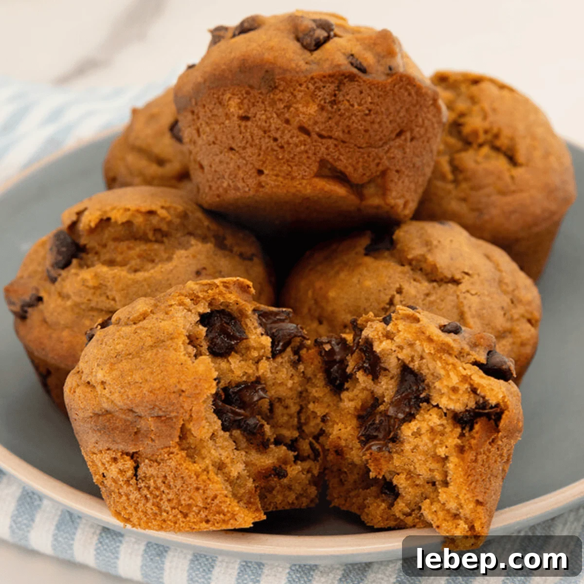 Large-Batch Pumpkin Chocolate Chip Muffins Recipe 6 pumpkin chocolate chip muffins on a plate one is opened up