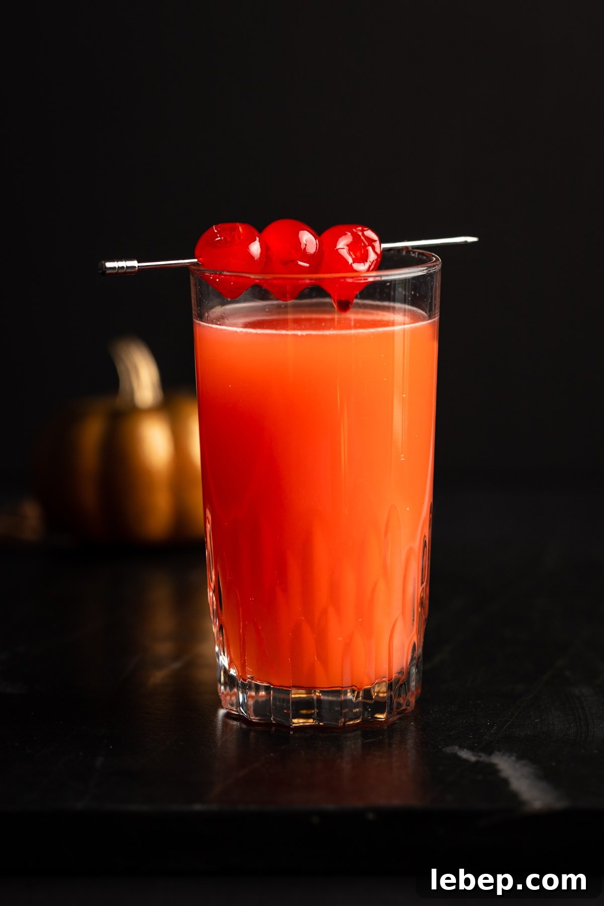 How to Make a Red Devil Cocktail: Recipe & Serving Tips 2 Eye level view of a the halloween cocktail, on a black marble table, with a pumpkin in the background.