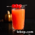 Red devil drink garnished with maraschino cherries, on a black marble table.