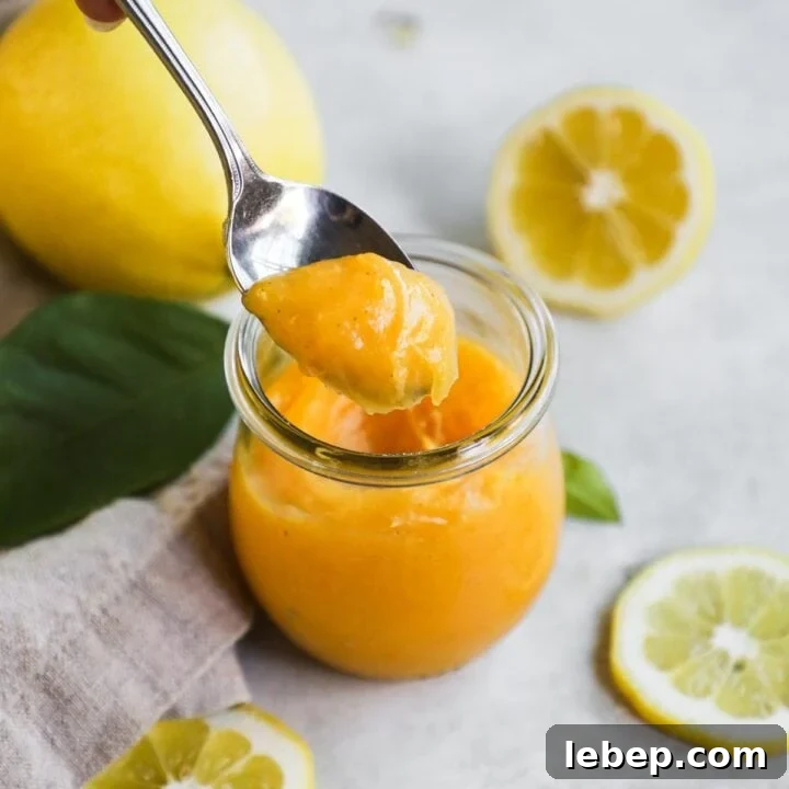 Spoon holding easy lemon curd with vanilla bean paste from a glass jar.