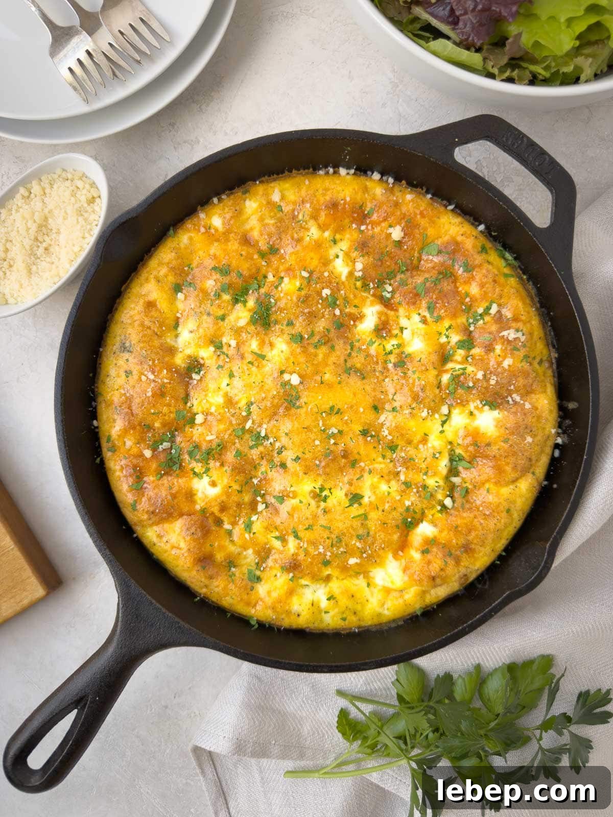 A golden puffed ham and cheese frittata in a cast iron skillet with parmesan on the side.