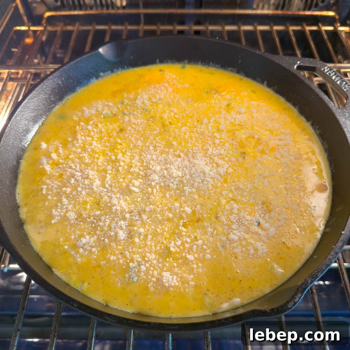 A golden frittata in a cast iron skillet going into the oven topped with parmesan cheese.