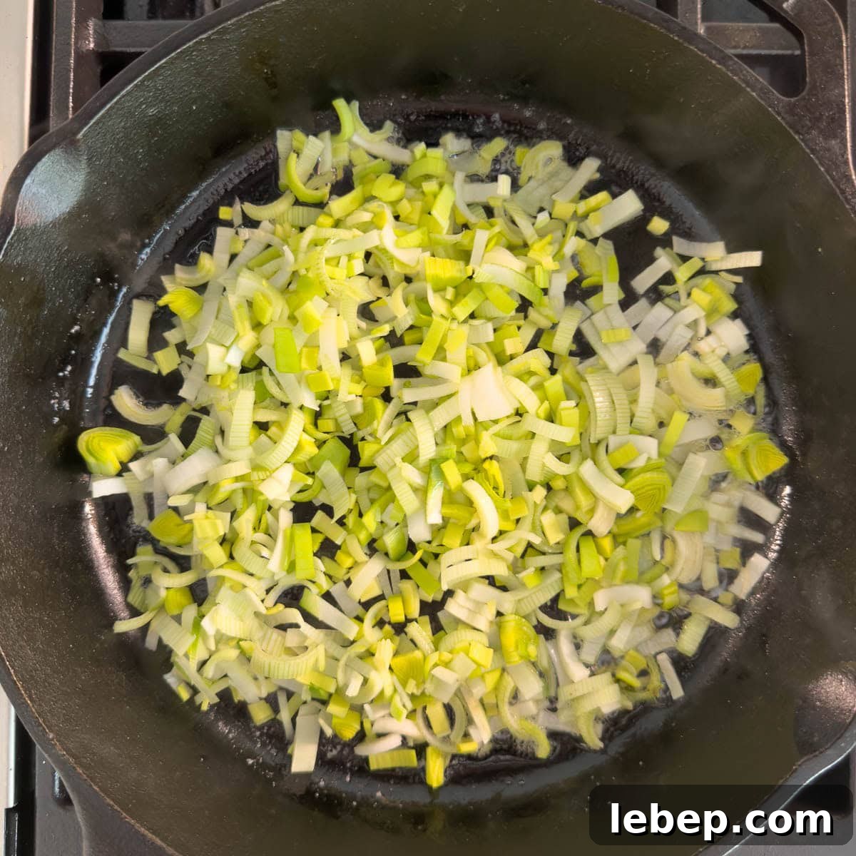 Cast iron skillet with chopped leeks cooking in butter on the stovetop.