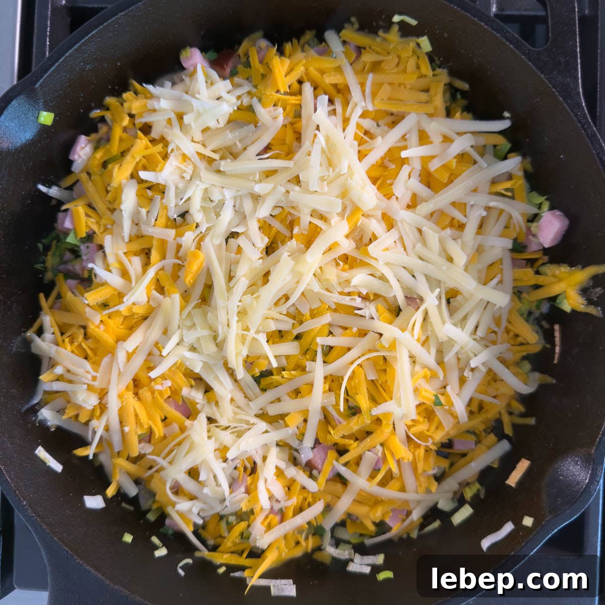 Cast iron pan showing orange and white grated cheese layer for a frittata.