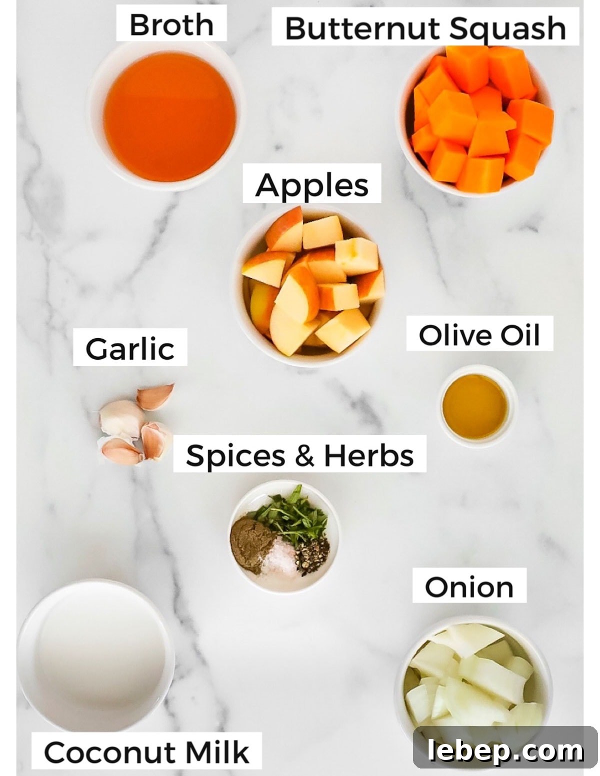 Labeled ingredients in small white bowls including: broth, butternut squash, apples, olive oil, garlic, spices and herbs, onion, and coconut milk