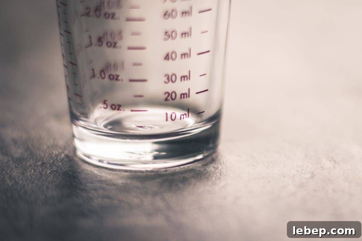 Cooking Measurement Guide: Key Conversions for Accurate Results 3 A close-up of a clear glass measuring cup on a gray surface, showing red measurement markings in milliliters and ounces, with the numbers clearly visible and the focus on the lower part of the cup.