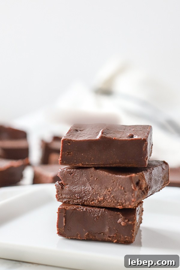 vegan fudge stacked 3 tall on a white plate with a white and black towel and more fudge pieces behind it