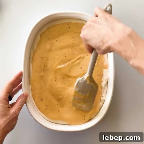 Spreading the blended peach ice cream mixture over the vanilla layer in the dish.
