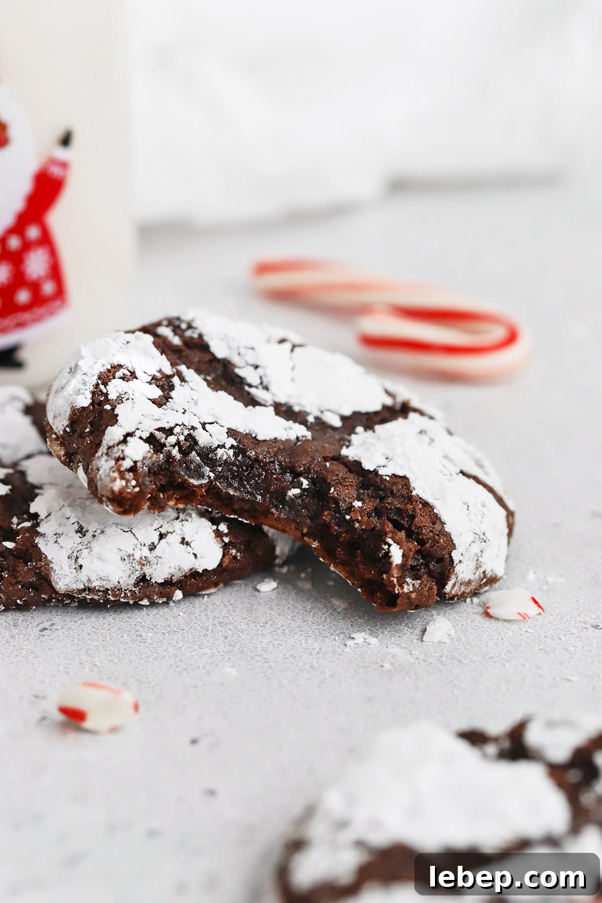Gluten-Free Peppermint Chocolate Crinkle Cookies Recipe 12 Front view of gluten-free peppermint chocolate crinkle cookies. One cookie has a bite out of it revealing a fudgy center.