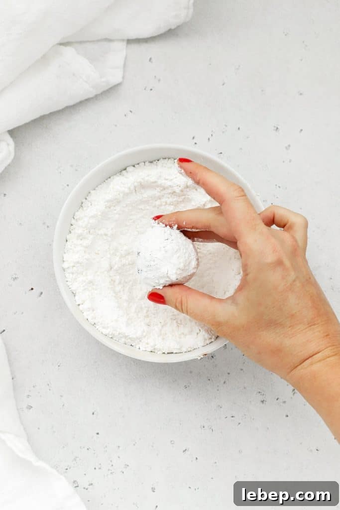 Gluten-Free Peppermint Chocolate Crinkle Cookies Recipe 9 Rolling balls of peppermint chocolate crinkle cookie dough in powdered sugar