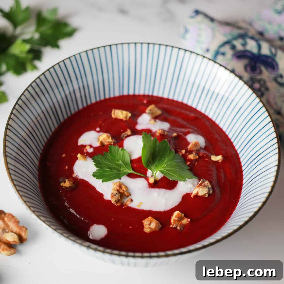 photo of a blue and white striped bowl with deep pink beetroot and walnut soup and dotted with coconut cream, walnut pieces and a sprig of parsley.