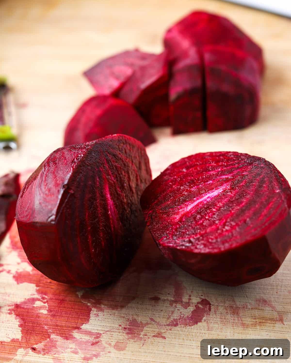 Photo of a peeled beetroot cut in half with some chopped beetroot in the background, on a wooden chopping board stained with beetroot juices.
