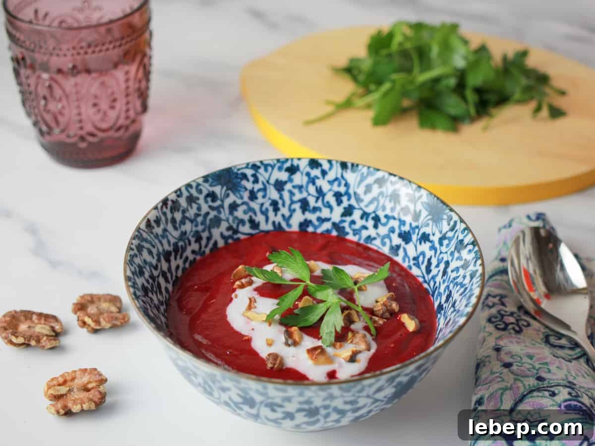 Bowl of Roasted Beetroot and Walnut Soup with coconut cream drizzle and walnuts and parsley sprinkled on top, with a chopping board of parsley in the background.