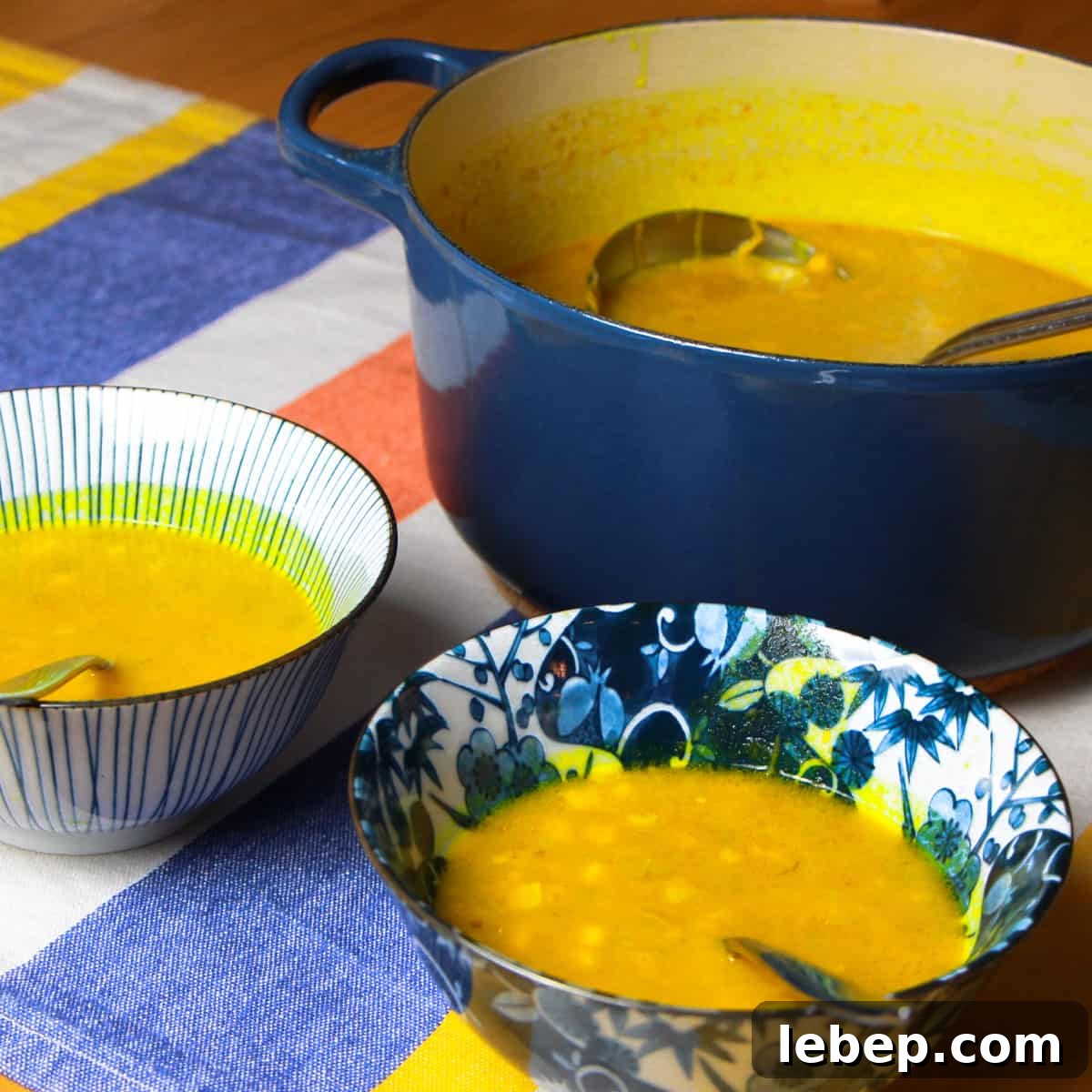 a big navy le creuset pot full of spiced pumpkin and sweetcorn soup with two bowls of soup in the foreground.