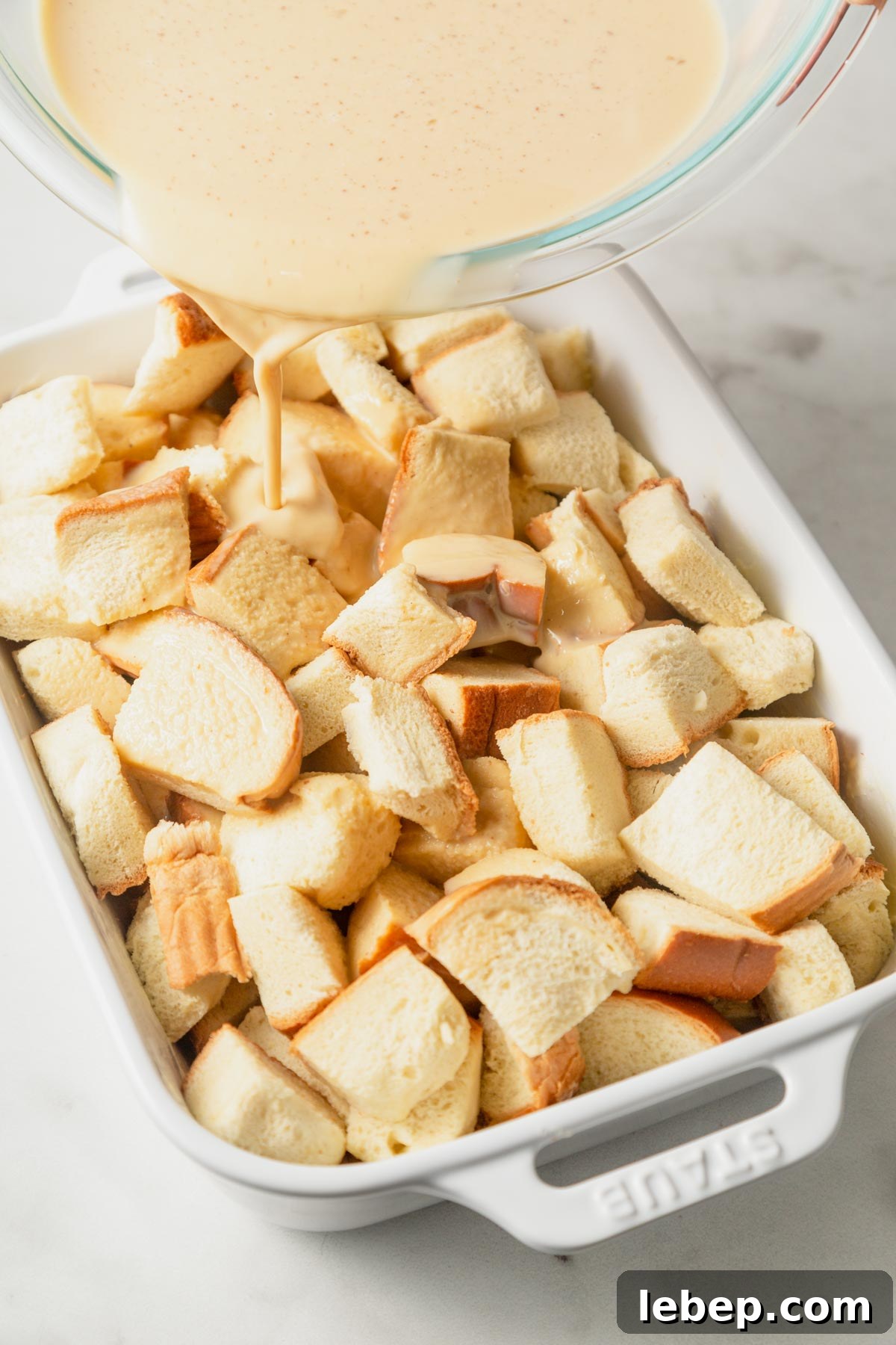 Brioche French Toast Casserole Recipe for Brunch or Holidays 8 pouring egg mixture on the cubed brioche bread.