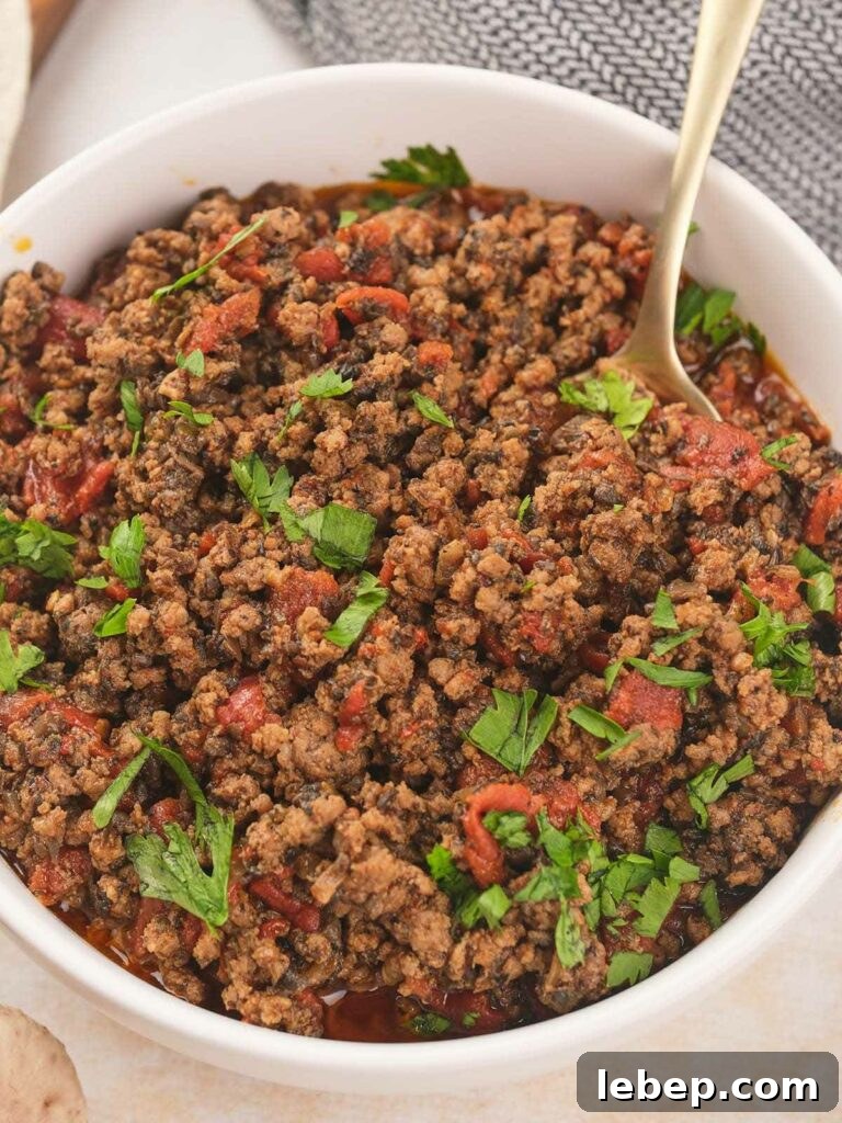 A white bowl of cooked meat garnished with fresh cilantro with a spoon inside.