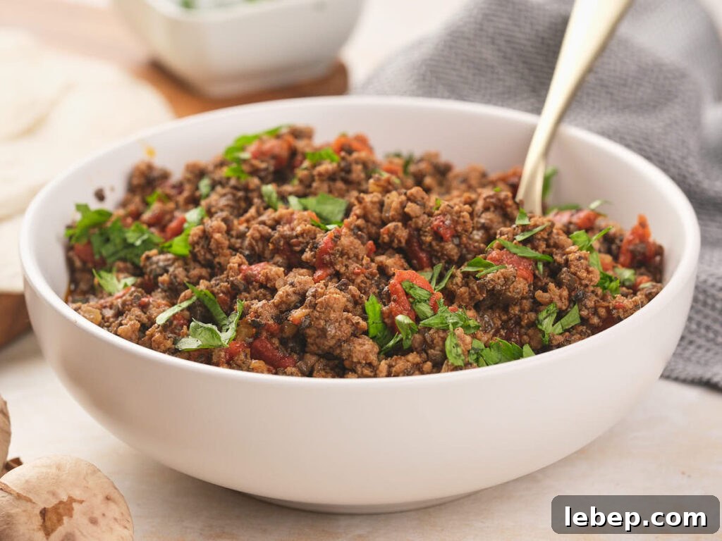 A bowl of seasoned ground beef garnished with fresh cilantro with a spoon inside.