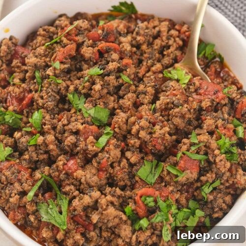 A white bowl of cooked meat garnished with fresh cilantro with a spoon inside.
