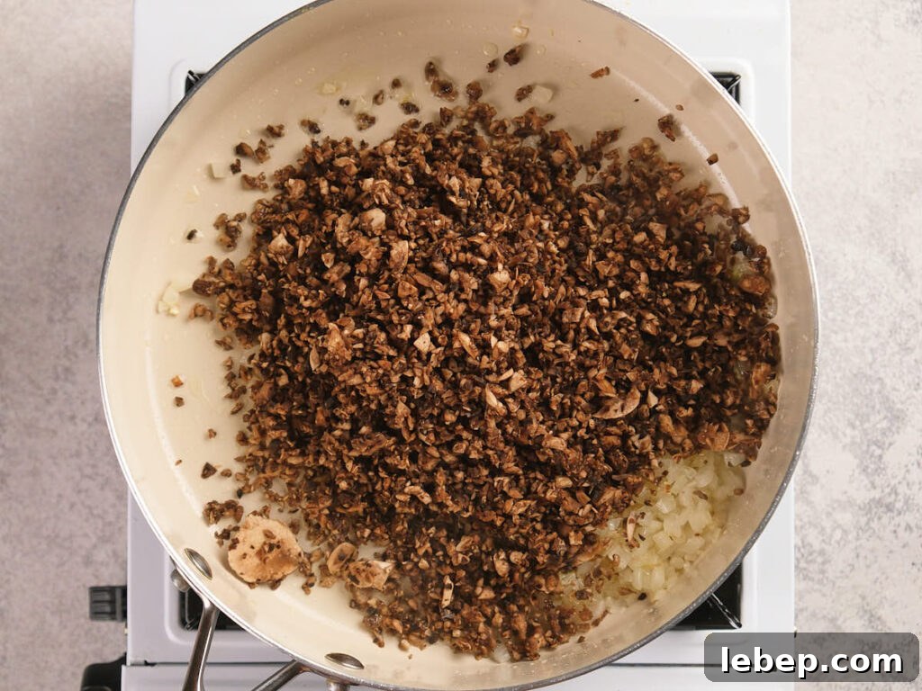A white skillet filled with cooked mushrooms is cooking on a stovetop.