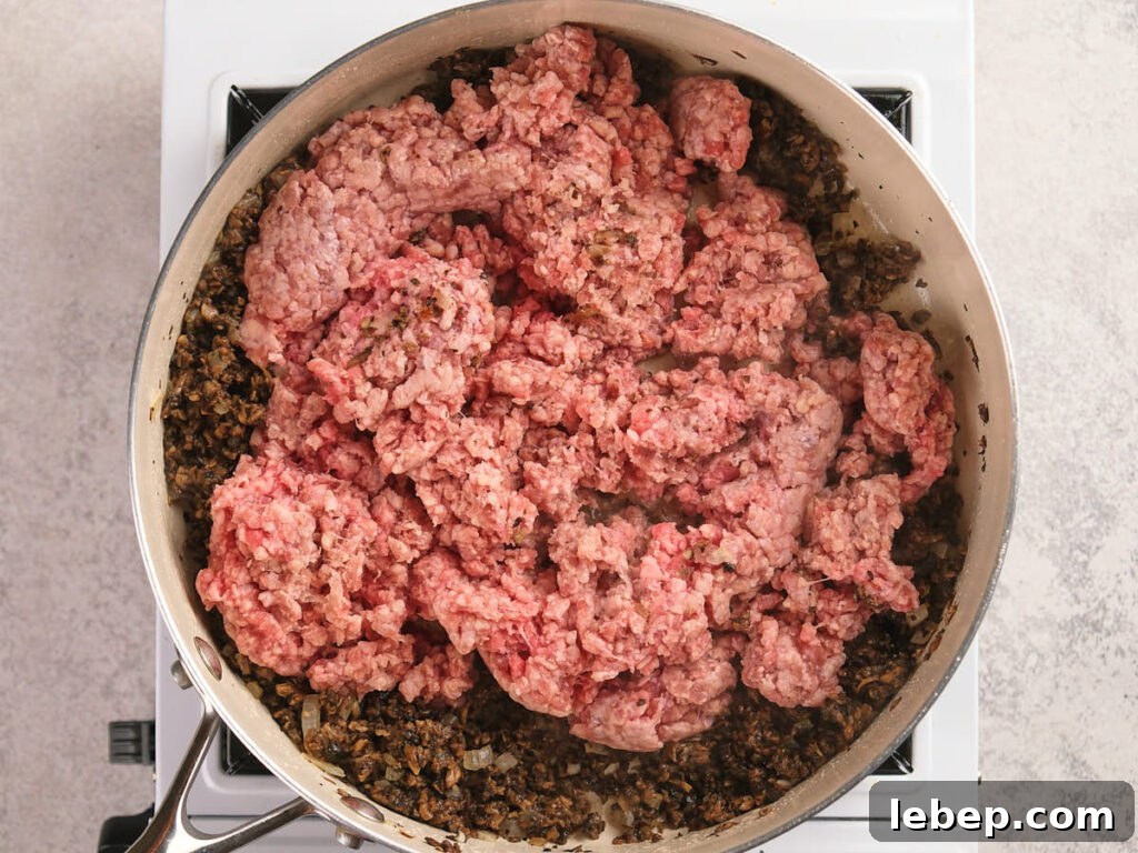 A skillet filled with sautéed mushrooms and ground beef in a stovetop.