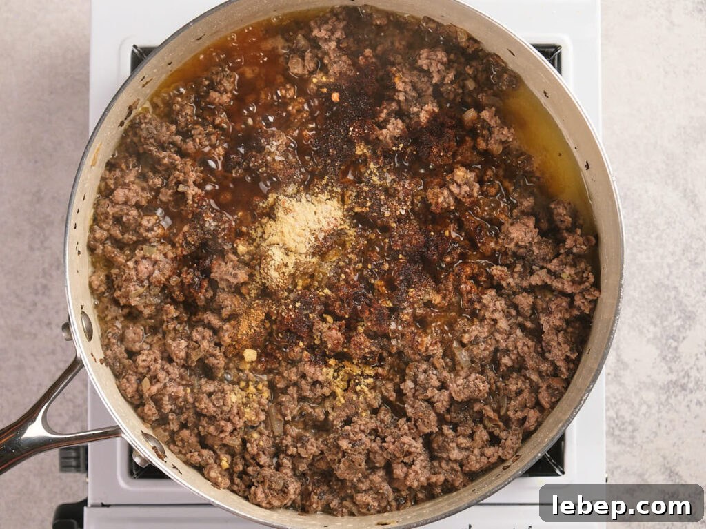 A simmering ground beef seasoned with spices in a white skillet on a stovetop.
