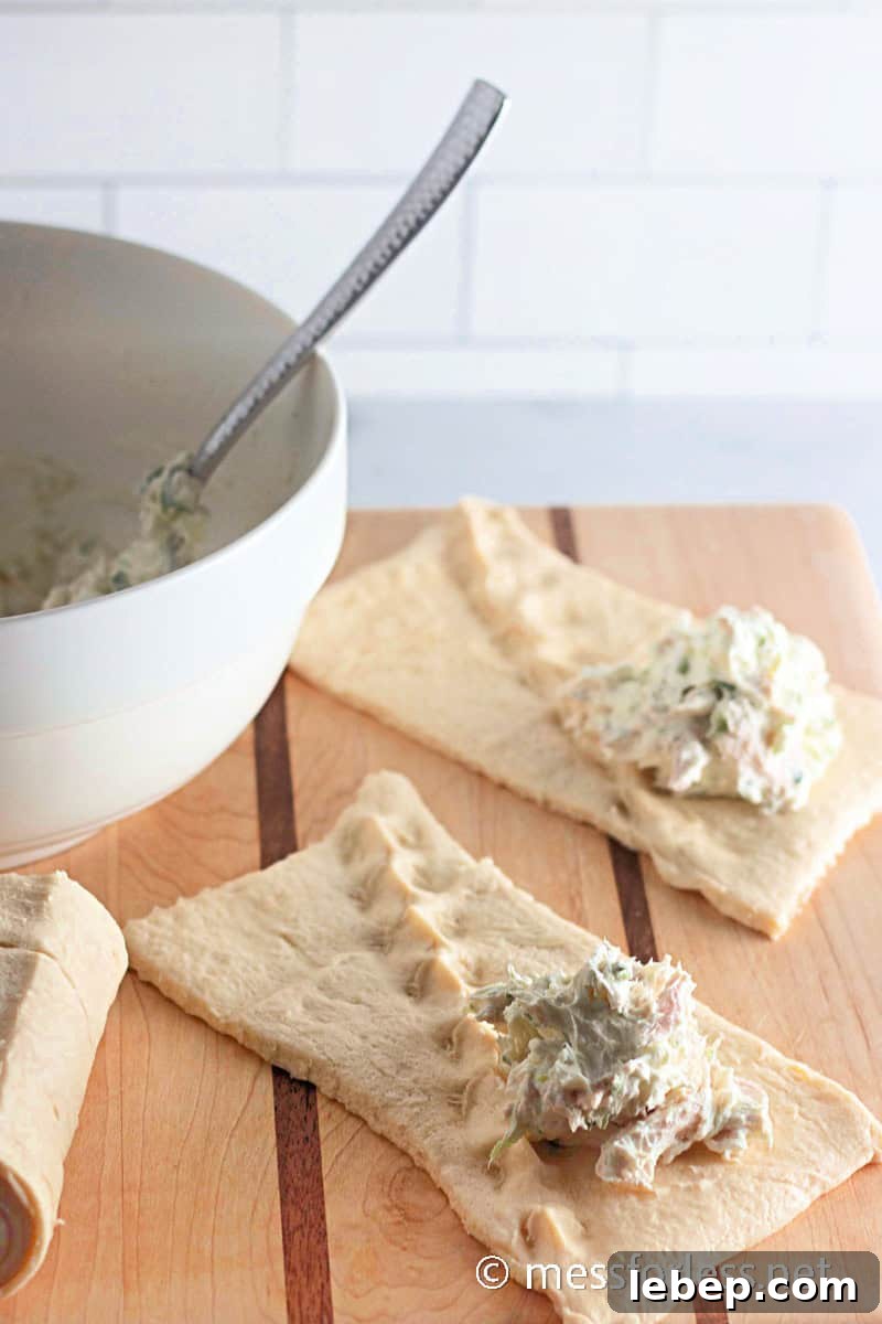 Cheesy Chicken Crescent Bake with Puff Pastry Squares 8 crescent dough on a wooden surface, each with a dollop of chicken mixture from a nearby white bowl, evoke the delightful essence of a Crescent Squares recipe.