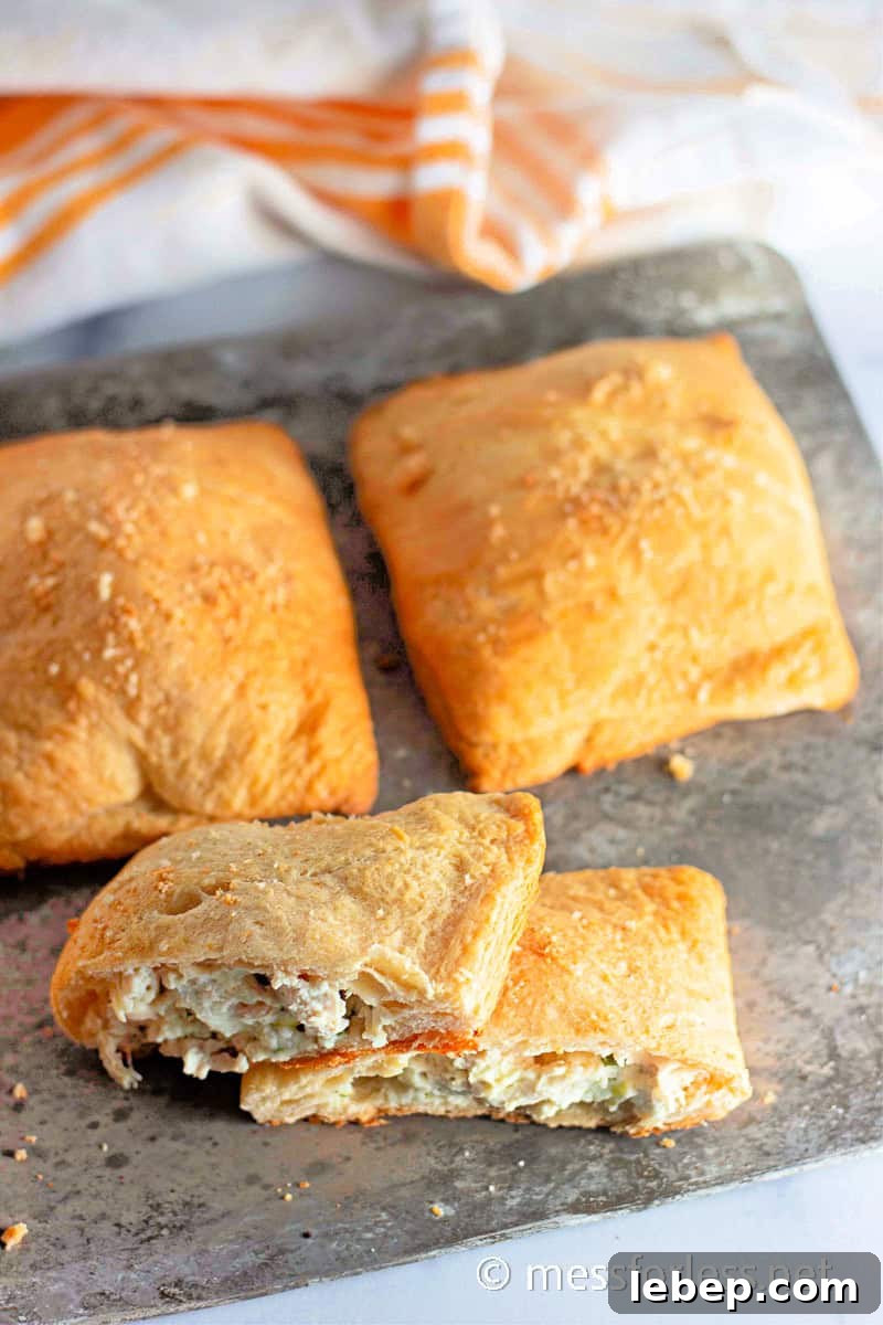 Cheesy Chicken Crescent Bake with Puff Pastry Squares 13 Four baked golden-brown chicken crescent squares rest on a metal tray, one of which is cut open to reveal a creamy filling. This delightful recipe combines flaky pastry with savory goodness.