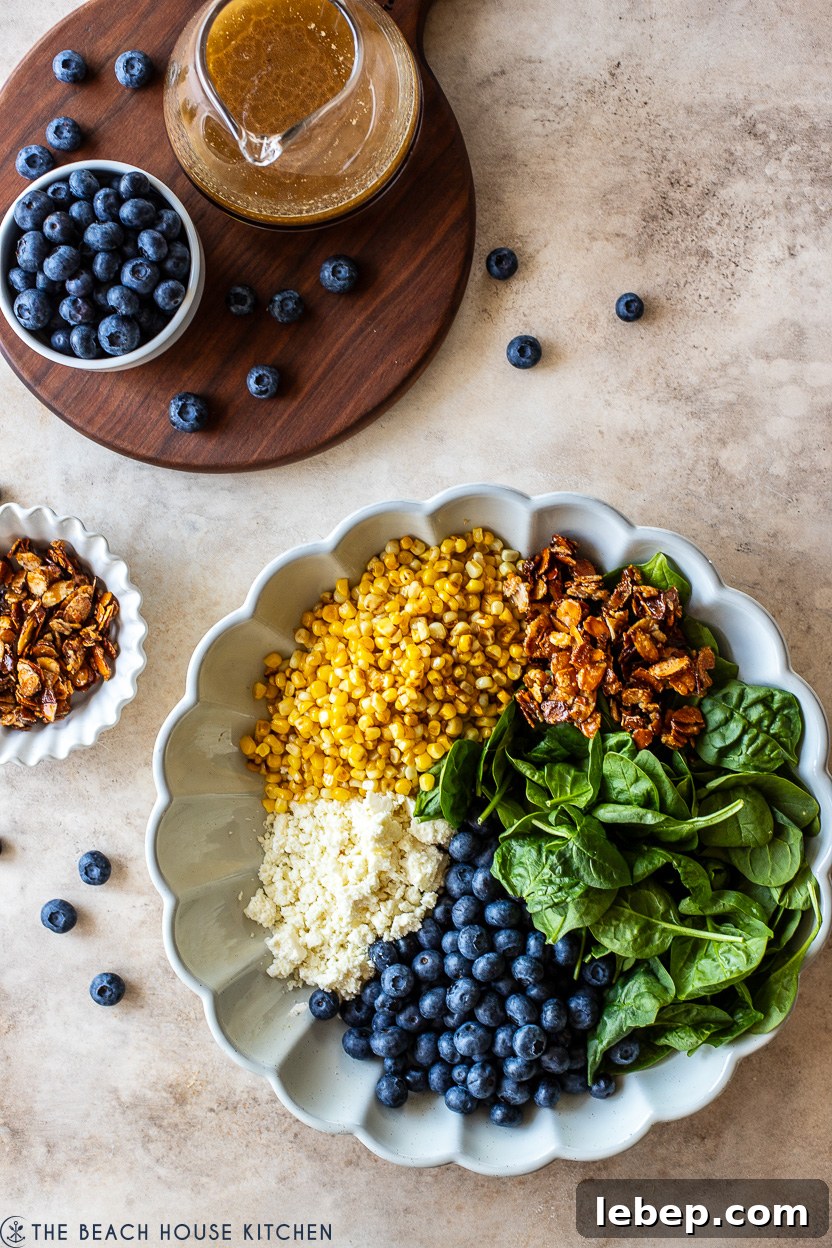 Overhead photo of a serving dish of corn, spinach leaves, blueberries, cotija cheese and candied almonds