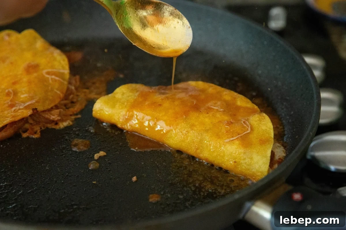 Spoon pouring sauce over a taco in a skillet to make chicken birria tacos.