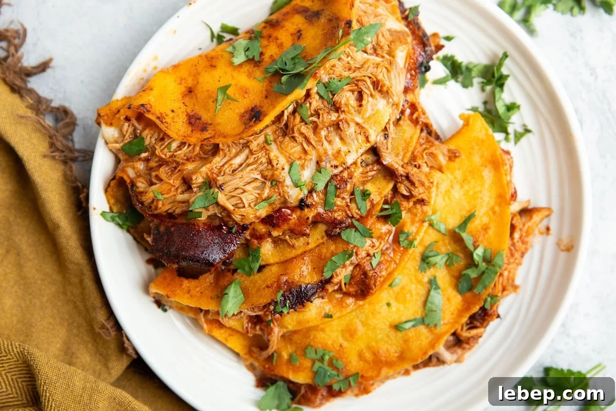 Chicken birria tacos on a plate sprinkled with chopped fresh cilantro and a golden napkin to the side.