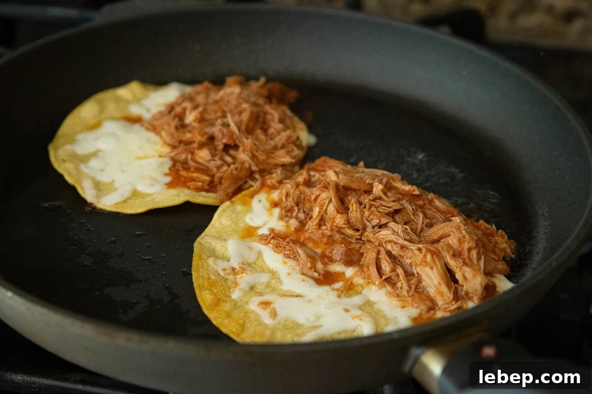 Two tacos with corn tortillas, cheese, and chicken cooking on a skillet to become crispy.