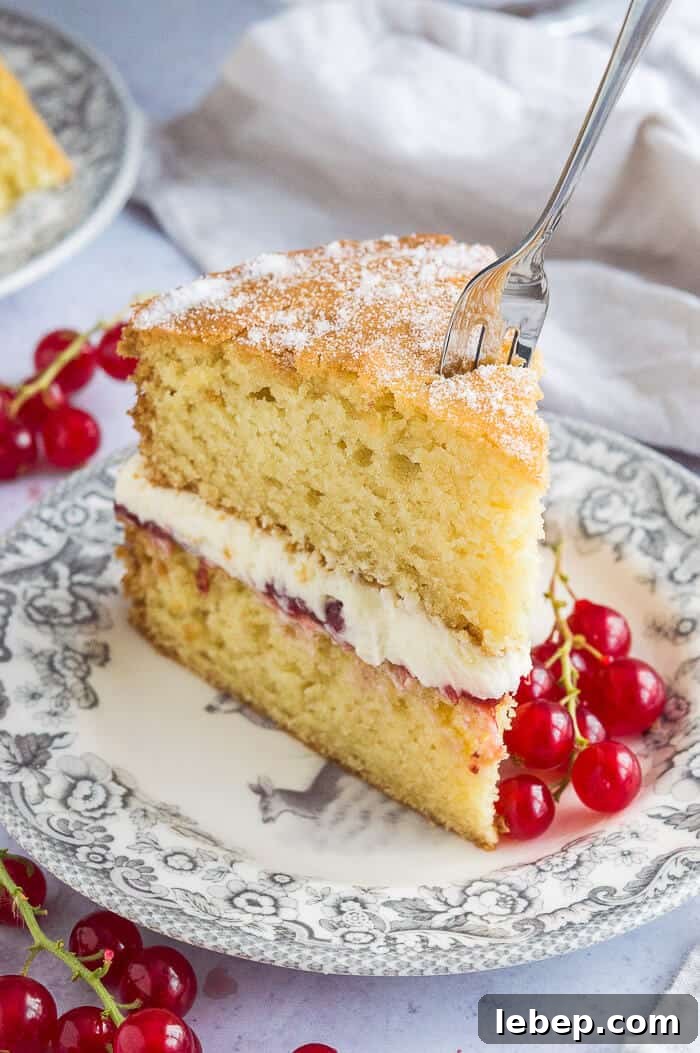 A slice of vegan Victoria sponge cake on a grey patterned plate with a fork sticking in it.